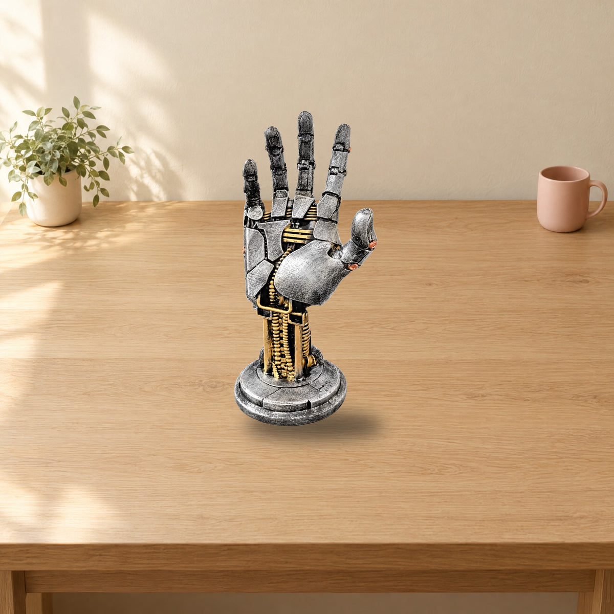 Silver mechanical hand stand on a sunlit wooden desk with a small plant and a pink mug